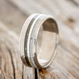 Shown here is "Cosmo", a custom, handcrafted men's wedding ring featuring a hammered band with iron ore, hammered silver, and elk antler inlays, upright facing left. Additional inlay options are available upon request.