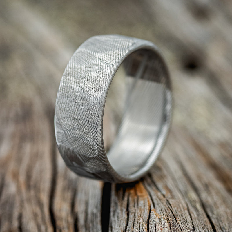 Shown here is a handcrafted men's wedding ring featuring a faceted Damascus steel band with an etched finish, upright facing left.