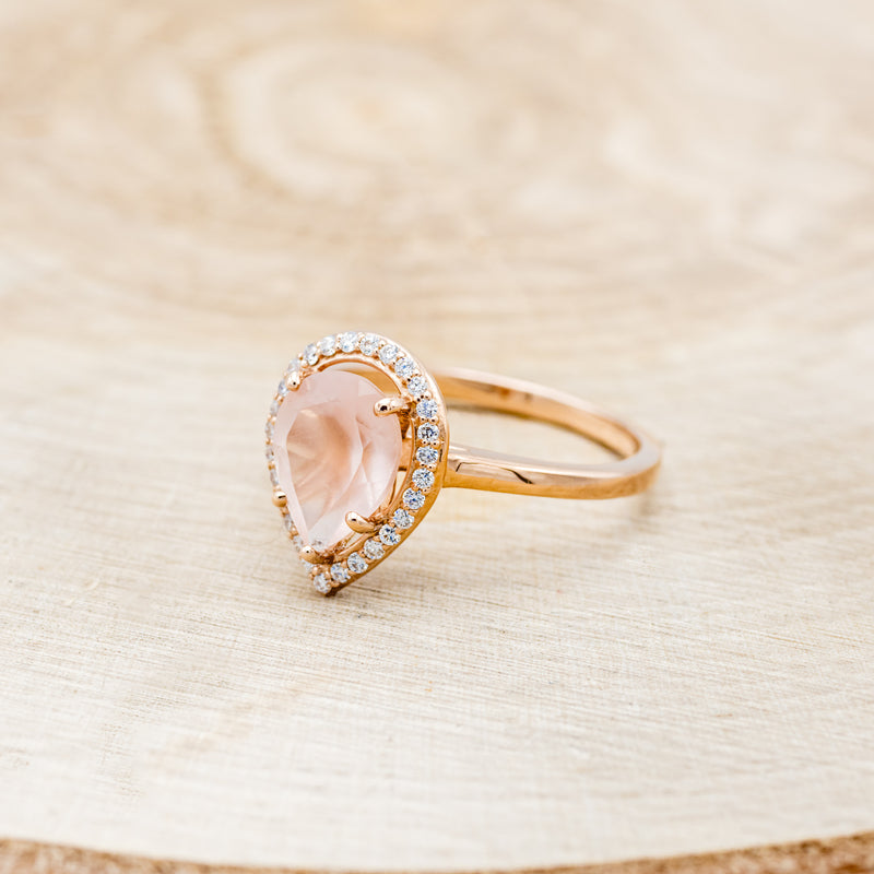 Shown here is "Clariss", a rose quartz women's engagement ring with a diamond halo, facing left. Many other center stone options are available upon request.