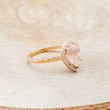Shown here is "Clariss", a rose quartz women's engagement ring with a diamond halo, facing right. Many other center stone options are available upon request.
