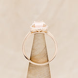 Shown here is "Clariss", a rose quartz women's engagement ring with a diamond halo, side view on stand. Many other center stone options are available upon request.