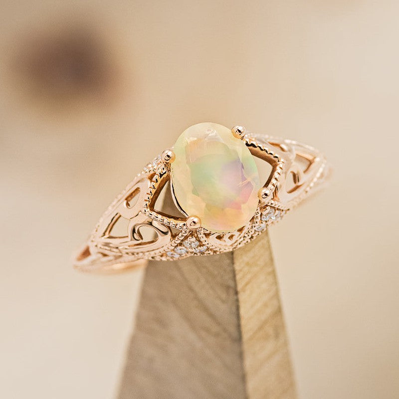 Shown here is "Relica", a vintage-style oval Welo opal women's engagement ring, on stand facing slightly right, with delicate and ornate details and is available with many center stone options