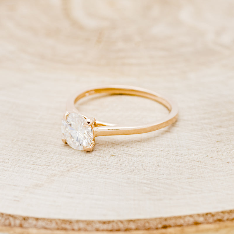 Shown here is a solitaire-style moissanite women's engagement ring with 4 claw prongs, facing left. Many other center stone options are available upon request.