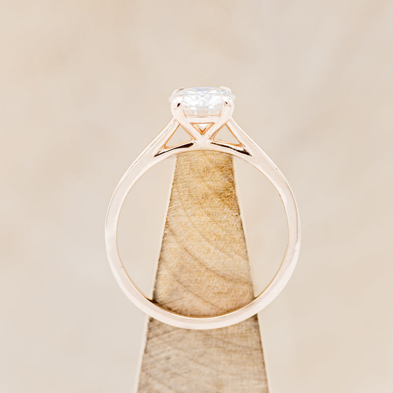 Shown here is a solitaire-style moissanite women's engagement ring with 4 claw prongs, side view on stand. Many other center stone options are available upon request.