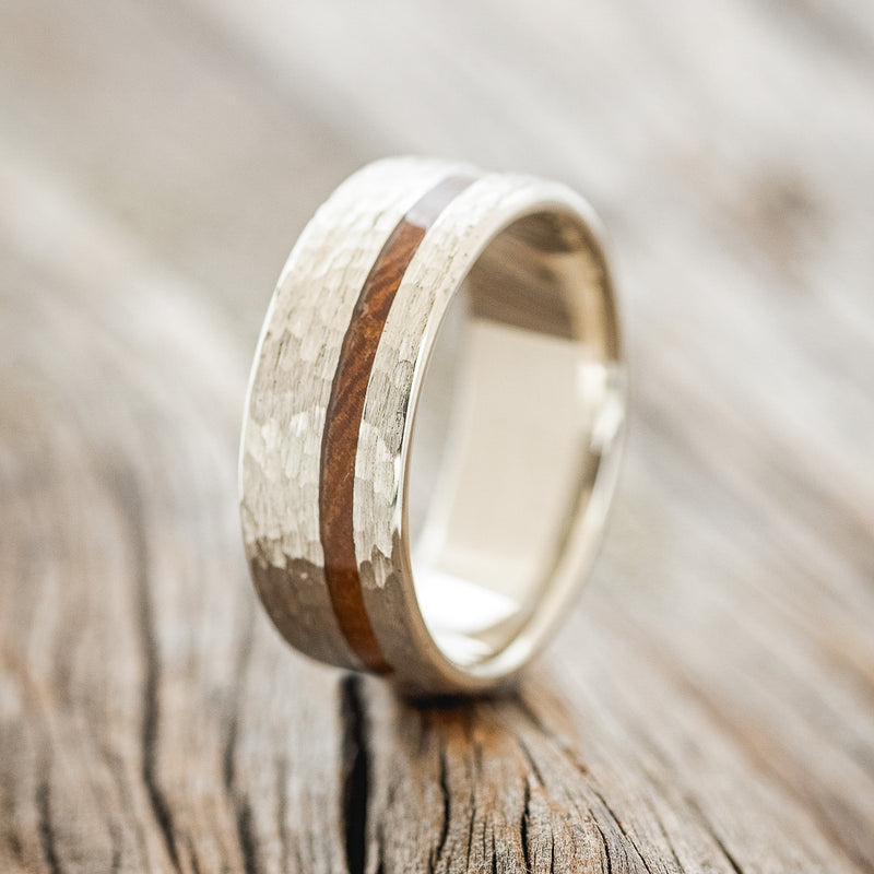 Shown here is "Vertigo", a custom, handcrafted men's wedding ring featuring an offset ironwood inlay with a hammered finish, upright facing left. Additional inlay options are available upon request.