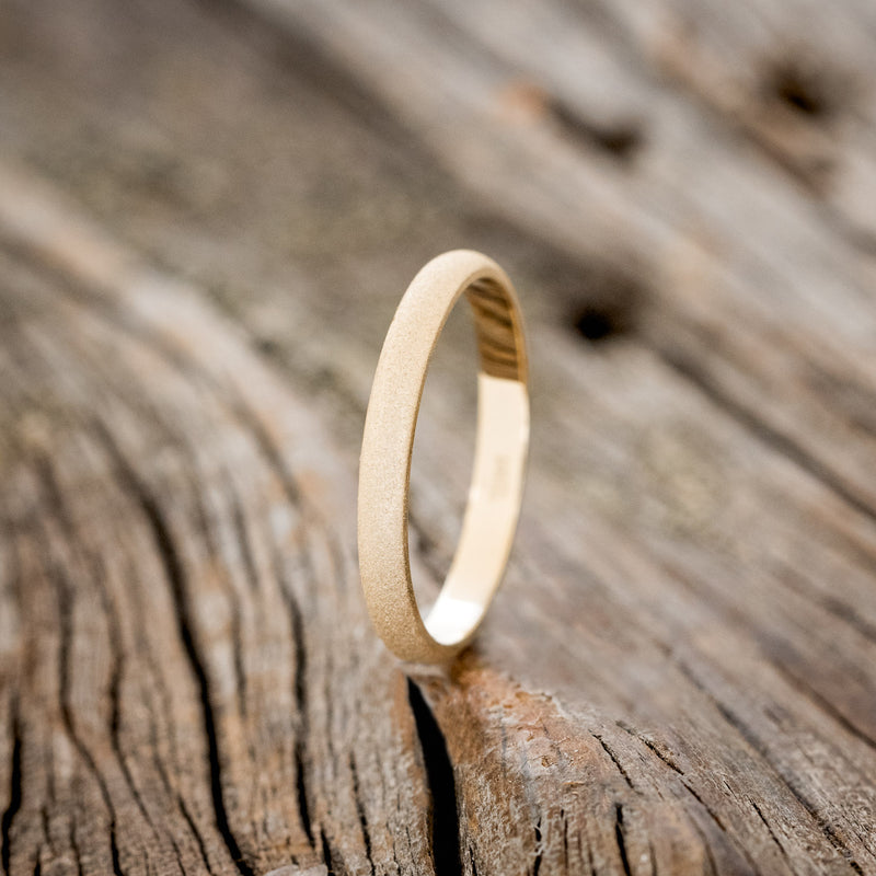 Shown here is a custom, handcrafted women's stacking band featuring a 14K gold band with a sandblasted finish, upright facing left.