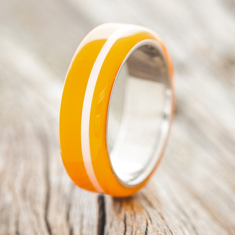 Shown here is "Remmy", a custom, handcrafted men's wedding ring featuring a hand-turned orange & white acrylic, upright facing left. Additional inlay options are available upon request.