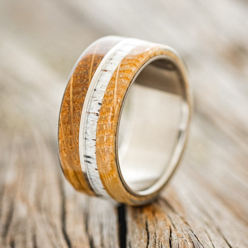 Shown here is "Golden", a custom, handcrafted men's wedding ring featuring whiskey barrel oak overlays and an antler inlays, upright facing left. Additional inlay and overlay options are available upon request.
