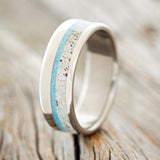 Shown here is "Tanner", a custom, handcrafted men's wedding ring featuring a turquoise and antler inlay on a titanium band, upright facing left. Additional inlay options are available upon request.