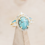 Shown here is "KB", a halo-style oval turquoise women's engagement ring with diamond accents and "Sama" tracer, on stand front facing. Many other center stone options are available upon request.