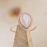 Shown here is "Terra", a halo-style Opal women's engagement ring, on stand facing slightly right, with delicate and ornate details and is available with many center stone options