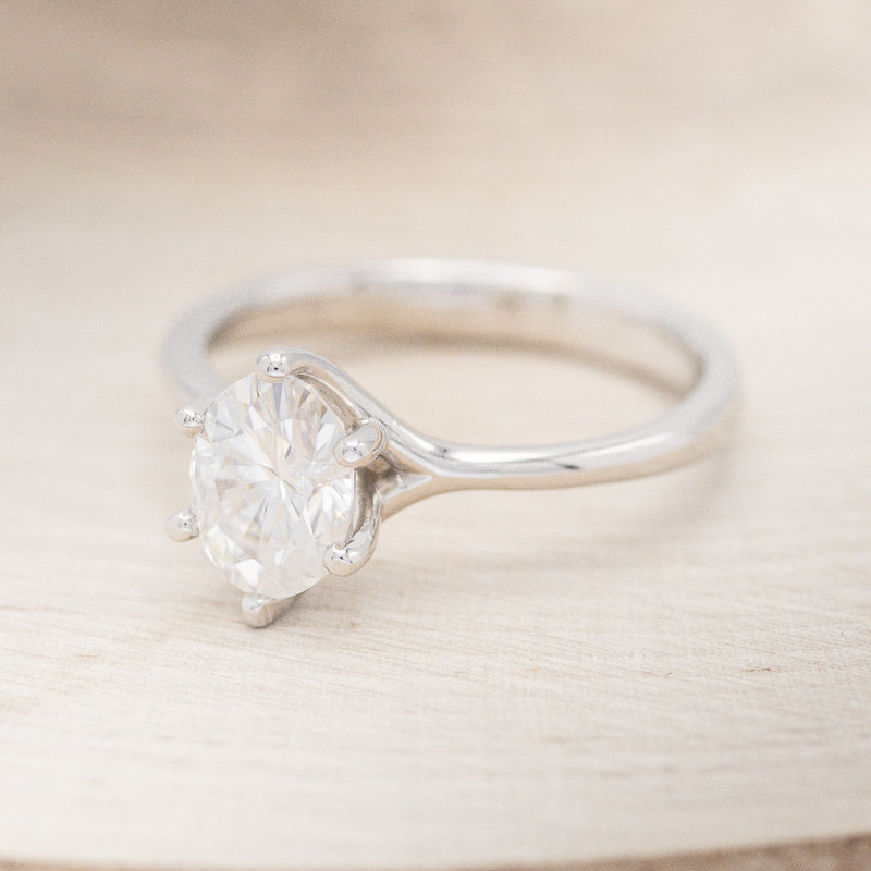 Shown here is "Tulip", a solitaire-style oval moissanite women's engagement ring with a split shank band, facing left. Many other center stone options are available upon request.