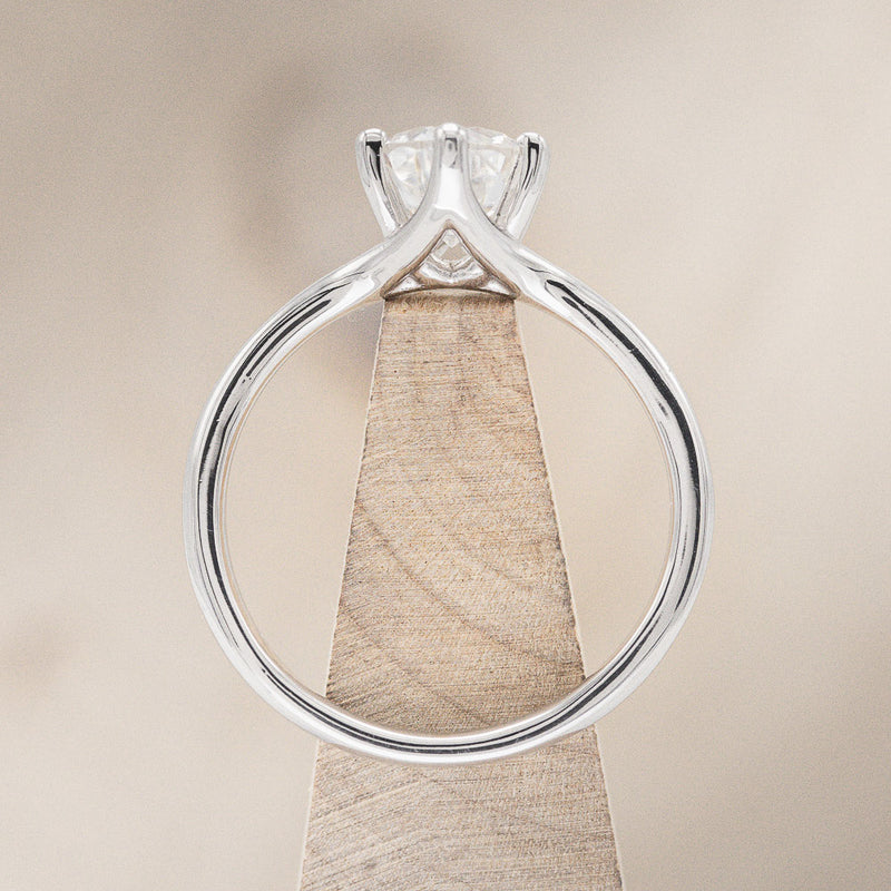 Shown here is "Tulip", a solitaire-style oval moissanite women's engagement ring with a split shank band, side view on stand. Many other center stone options are available upon request.