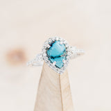 Shown here is "KB", a turquoise women's engagement ring with a diamond halo and diamond accents, on stand front facing. Many other center stone options are available upon request.