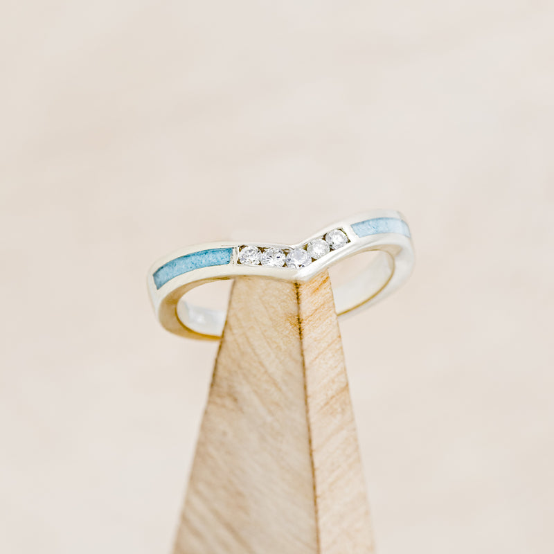 Shown here is "Kida", a custom, handcrafted women's stacking band featuring turquoise inlays and diamonds on a 14K gold band, on stand front facing. Additional inlay options are available upon request.