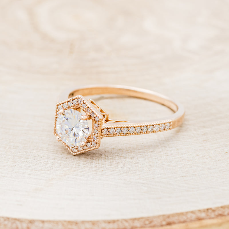 Shown here is "Odessa", a geometric-style moissanite women's engagement ring with a diamond halo and diamond accents, facing left. Many other center stone options are available upon request.