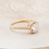 Shown here is "Odessa", a geometric-style moissanite women's engagement ring with a diamond halo and diamond accents, facing right. Many other center stone options are available upon request.