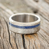 Shown here is "Vertigo", a custom, handcrafted men's wedding ring featuring a lapis lazuli inlay with a crosshatched finish, laying flat. Additional inlay options are available upon request.