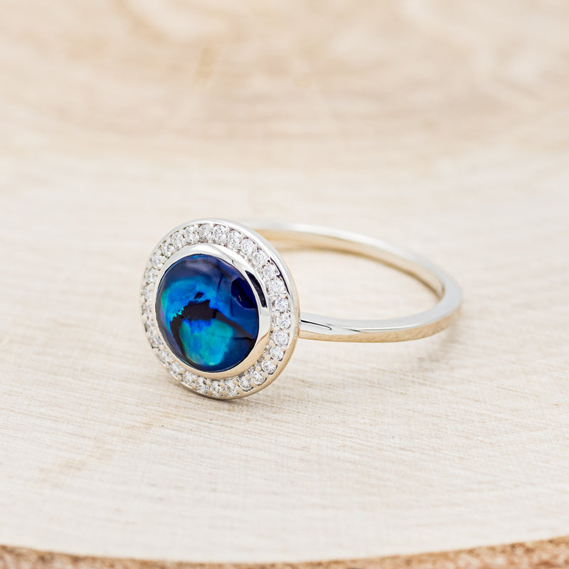 Shown here is "Terra", a round paua shell women's engagement ring with a diamond halo, facing left. Many other center stone options are available upon request.