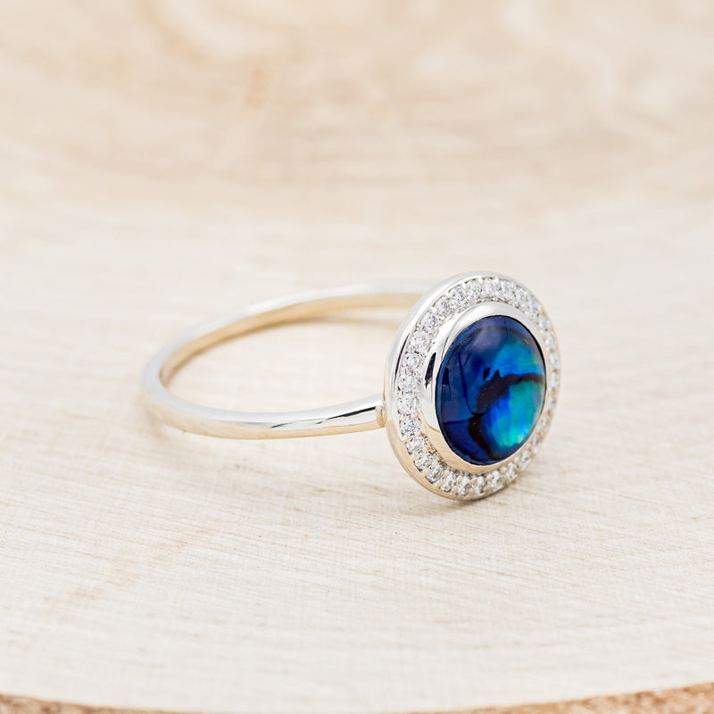 Shown here is "Terra", a round paua shell women's engagement ring with a diamond halo, facing right. Many other center stone options are available upon request.