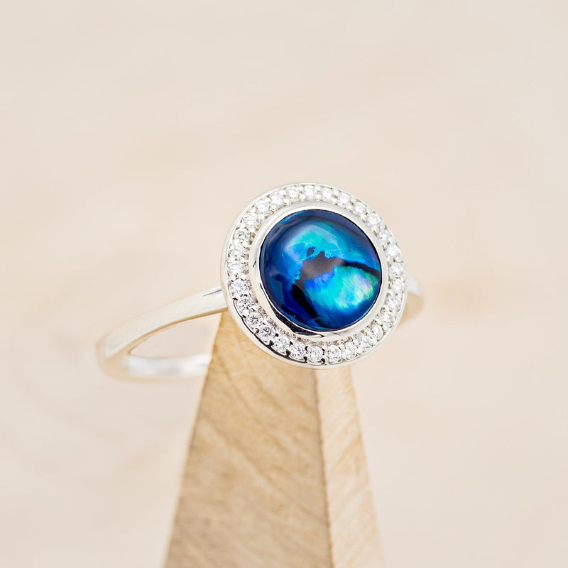 Shown here is "Terra", a round paua shell women's engagement ring with a diamond halo, on stand facing slightly right. Many other center stone options are available upon request. 