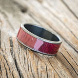 Shown here is "Rainier", a custom, handcrafted men's wedding ring featuring purpleheart wood inlay on a fire-treated black zirconium band, tilted left. Additional inlay options are available upon request.