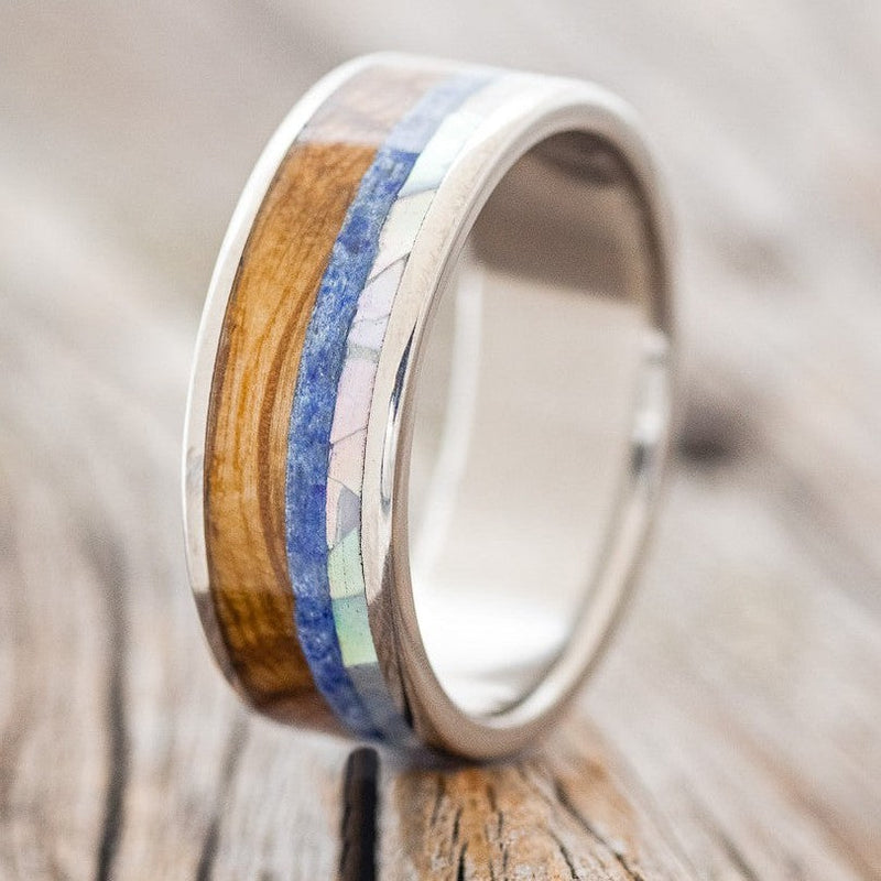 Shown here is "Rainier", a custom, handcrafted men's wedding ring featuring a mother of pearl, lapis lazuli, and whiskey barrel oak inlays, upright facing left. Additional inlay options are available upon request.