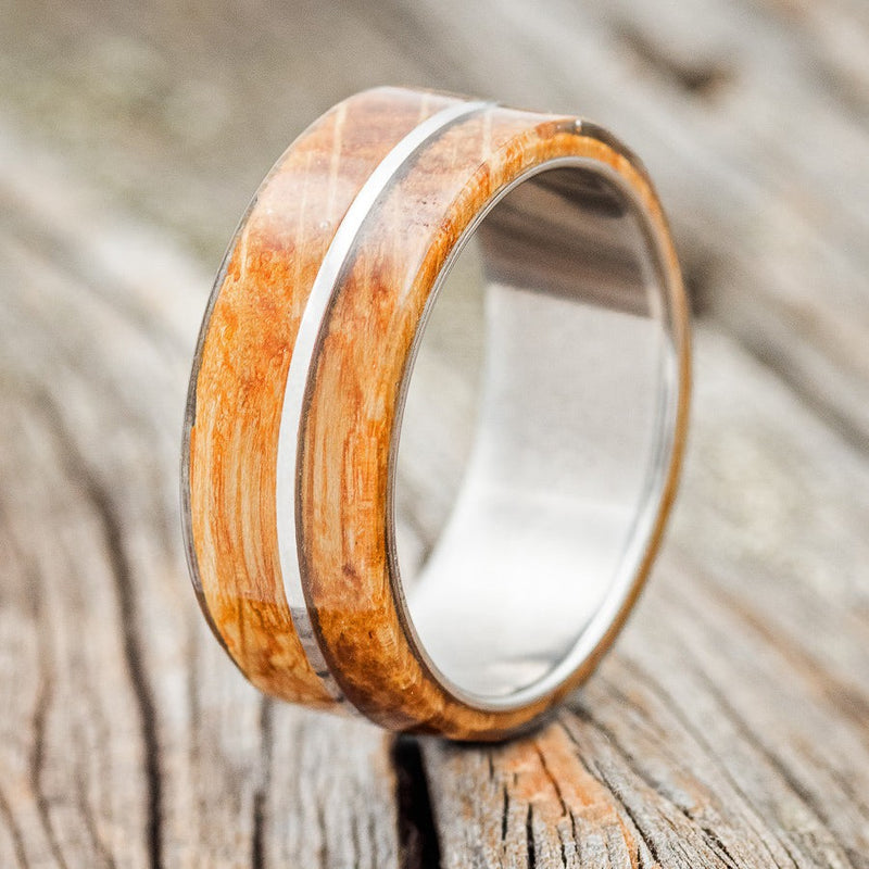 Shown here is "Golden", a handcrafted men's wedding ring featuring a whiskey barrel oak overlay divided by a titanium inlay, upright facing left. Additional inlay options are available upon request.