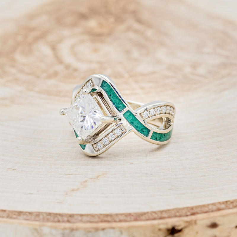 Shown here is "Helix", a geometric-style princess cut moissanite women's engagement ring with diamond accents and malachite inlays, facing left. Many other center stone options are available upon request.