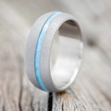 Shown here is "Vertigo", a custom, handcrafted men's wedding ring featuring a turquoise inlay with a sandblasted domed band, upright facing left. Additional inlay options are available upon request.