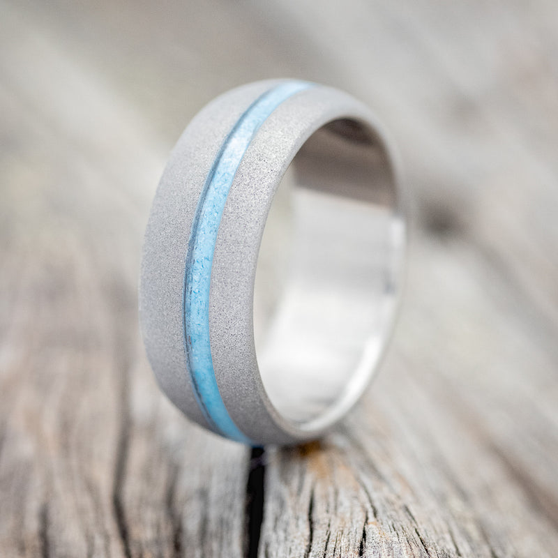Shown here is "Vertigo", a handcrafted men's wedding ring featuring a turquoise inlay with a sandblasted domed band, upright facing left.