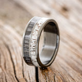 Shown here is "Dyad", a custom, handcrafted men's wedding ring featuring 2 channels with grey birch wood and antler inlays, upright facing left.