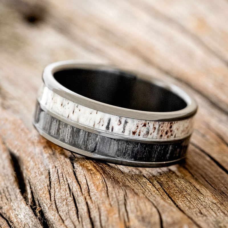 Shown here is "Dyad", a custom, handcrafted men's wedding ring featuring 2 channels with grey birch wood and antler inlays, tilted left.