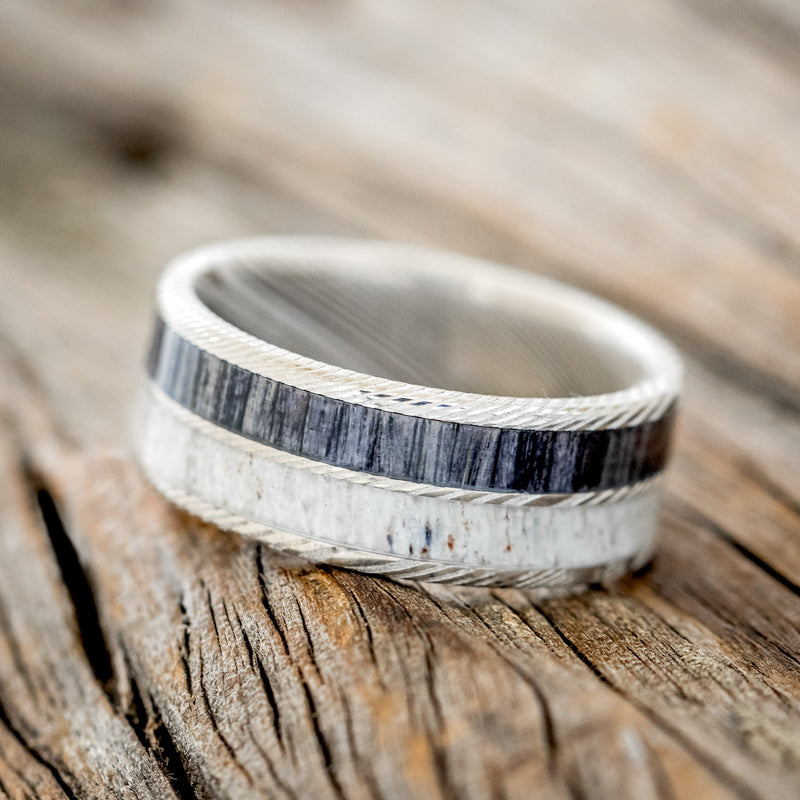 Shown here is "Dyad", a custom, handcrafted men's wedding ring featuring 2 channels with grey birch wood and antler inlays, tilted left. Additional inlay options are available upon request.