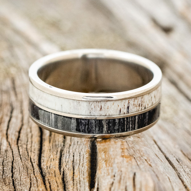 Shown here is "Dyad", a custom, handcrafted men's wedding ring featuring 2 channels with grey birch wood and antler inlays, laying flat.