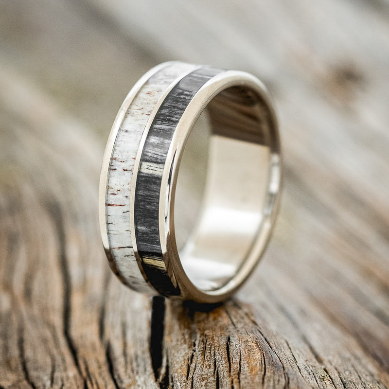 Shown here is "Dyad", a custom, handcrafted men's wedding ring featuring 2 channels with grey birch wood and antler inlays, upright facing left.