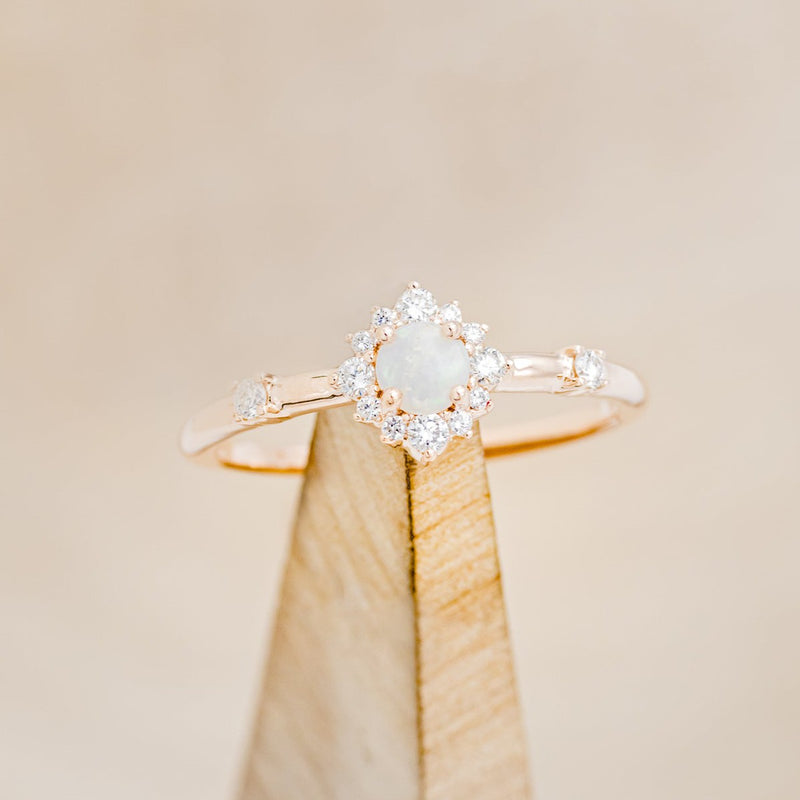Shown here is "Starla", a round cut opal women's engagement ring with a starburst diamond halo, on stand front facing. Many other center stone options are available upon request. 