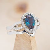 Shown here is a halo-style lab-created alexandrite women's engagement ring with tracer, on stand facing slightly right, with delicate and ornate details and is available with many center stone options