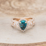 Shown here is "Loretta", a split shank-style turquoise women's engagement ring with a diamond halo and leaf-shape diamond accents, front facing. Many other center stone options are available upon request.