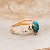 Shown here is "Loretta", a split shank-style turquoise women's engagement ring with a diamond halo and leaf-shape diamond accents, facing right. Many other center stone options are available upon request.