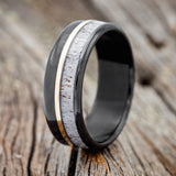 Shown here is "Tanner", a custom, handcrafted men's wedding ring featuring a naturally shed elk antler overlay and a 14K yellow gold inlay, shown here on a fire-treated black zirconium band, upright facing left. Additional inlay options are available upon request.