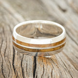 Shown here is "Silas", a handcrafted men's wedding ring featuring two whiskey barrel wood inlays on a domed profile silver band, laying flat. Additional inlay options are available upon request.