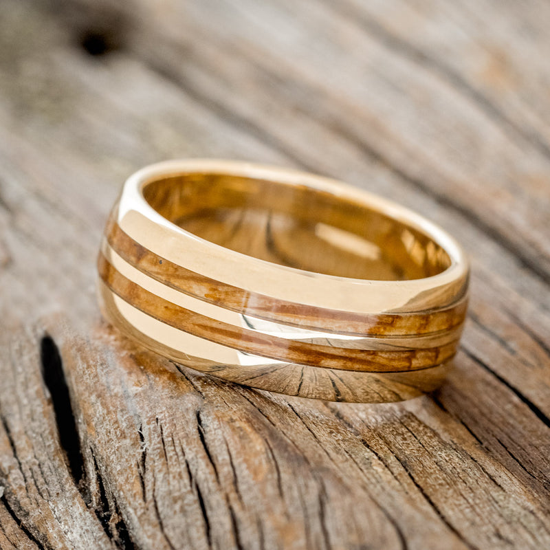 Shown here is "Silas", a handcrafted men's wedding ring featuring two whiskey barrel wood inlays on a domed profile band, tilted left. Additional inlay options are available upon request.
