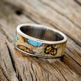 Shown here is "Rainier", a custom, handcrafted men's wedding ring featuring buckeye burl wood, with hand-crushed turquoise and gold nuggets filling the knots and burl holes, tilted left.