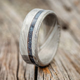 Shown here is "Vertigo", a custom, handcrafted men's wedding ring featuring a patina copper inlay on a Damascus steel band, upright facing left. Additional inlay options are available upon request.