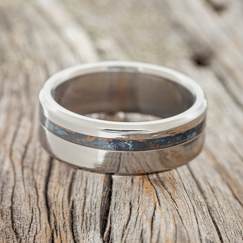 Shown here is "Vertigo", a custom, handcrafted men's wedding ring featuring a patina copper inlay, laying flat. Additional inlay options are available upon request.