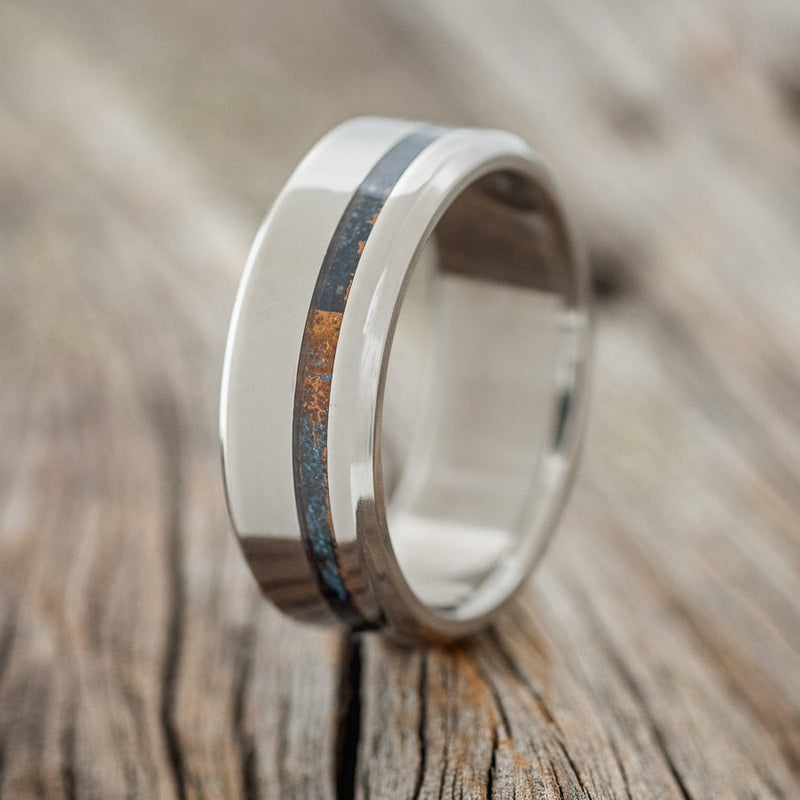 Shown here is "Vertigo", a custom, handcrafted men's wedding ring featuring a patina copper inlay, shown here in a titanium band, upright facing left. Additional inlay options are available upon request.
