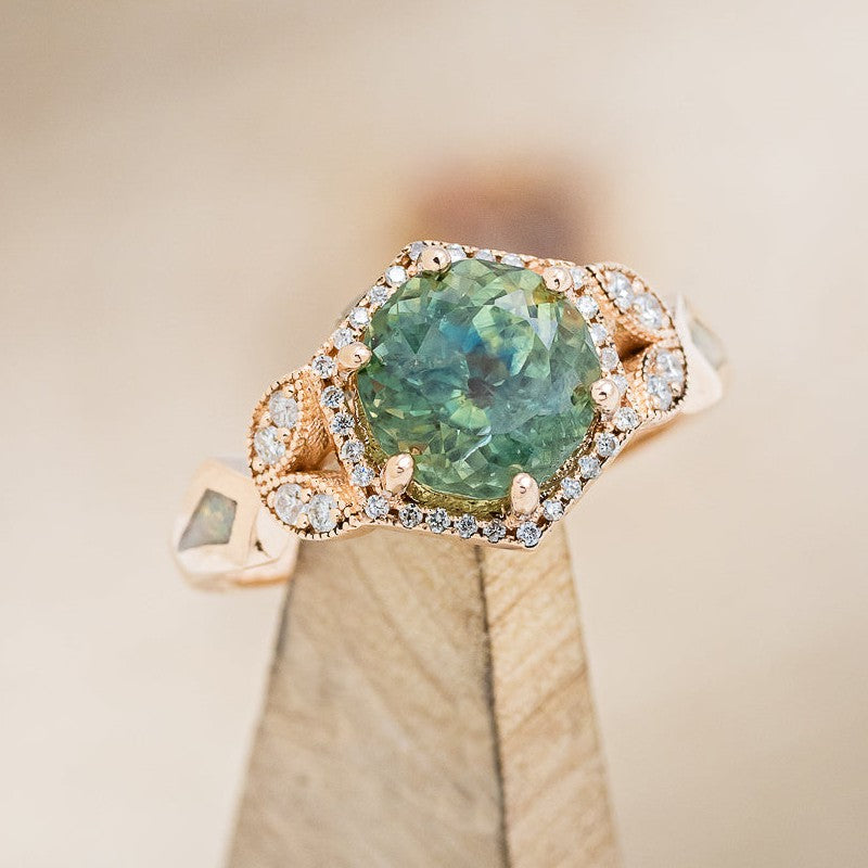 Shown here is "Lucy in the Sky", a halo-style Montana sapphire women's engagement ring with diamond accents and fire & ice opal inlays, on stand facing slightly right. Many other center stone options are available upon request.