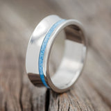 Shown here is "Vertigo", a custom, handcrafted concave men's wedding ring featuring a turquoise inlay, upright facing left. Additional inlay options are available upon request.