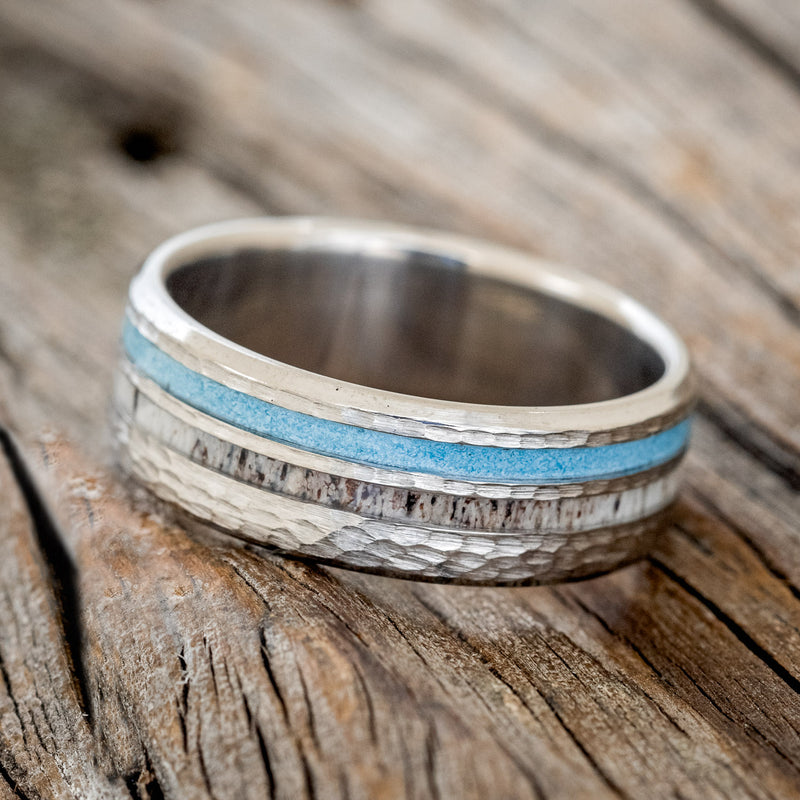 Shown here is "Cosmo", a custom, handcrafted men's wedding ring featuring elk antler and hand-crushed turquoise inlays on a hammered band, tilted left.
